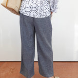 Person wearing a white shirt with black geometric pattern and gray wide-leg pants, standing on a brown floor.
