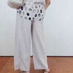 Person wearing a patterned top and light-colored pants on a plain background