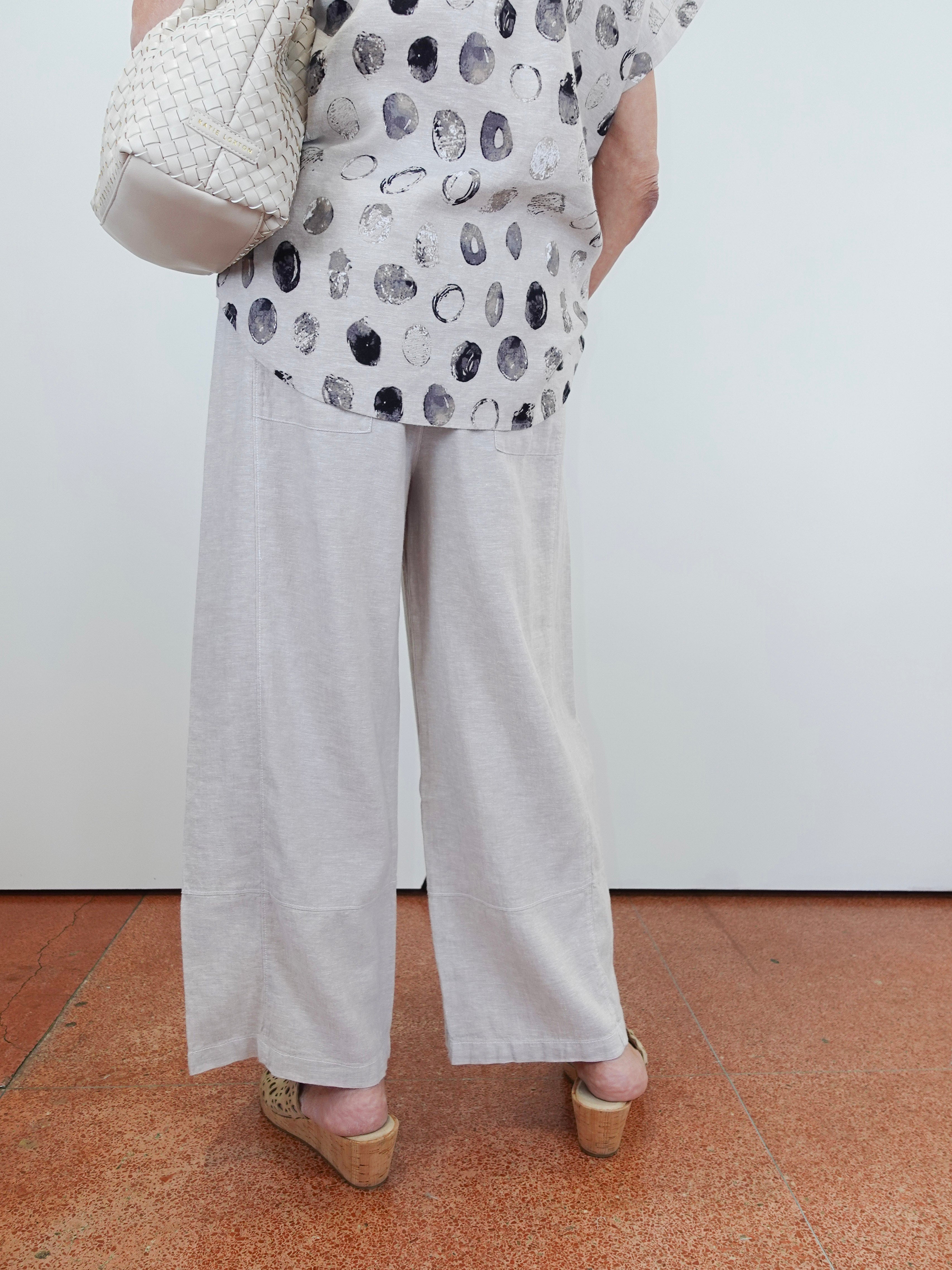 Person wearing a patterned top and light-colored pants on a plain background
