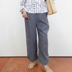 Person wearing a patterned shirt, gray pants, and sandals on a plain background