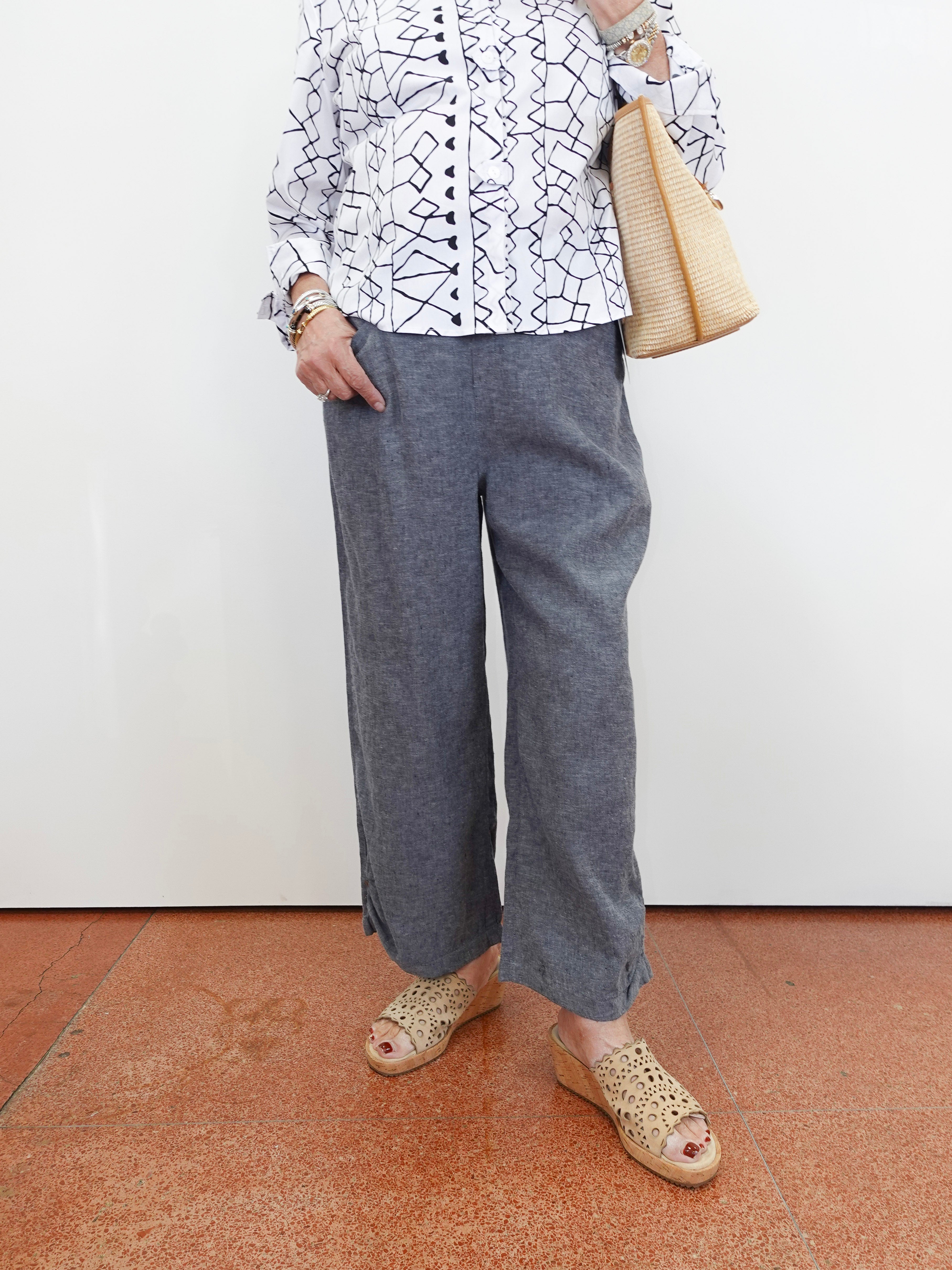 Person wearing a patterned shirt, gray pants, and sandals on a plain background