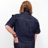 A person shown from the back wearing a dark indigo denim short-sleeve work shirt and matching denim pants against a plain white background.