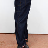 A person wearing dark indigo denim jeans with a relaxed straight-leg fit and black snakeskin-textured peep-toe block-heel mules, standing against a white wall on a terracotta tiled floor.