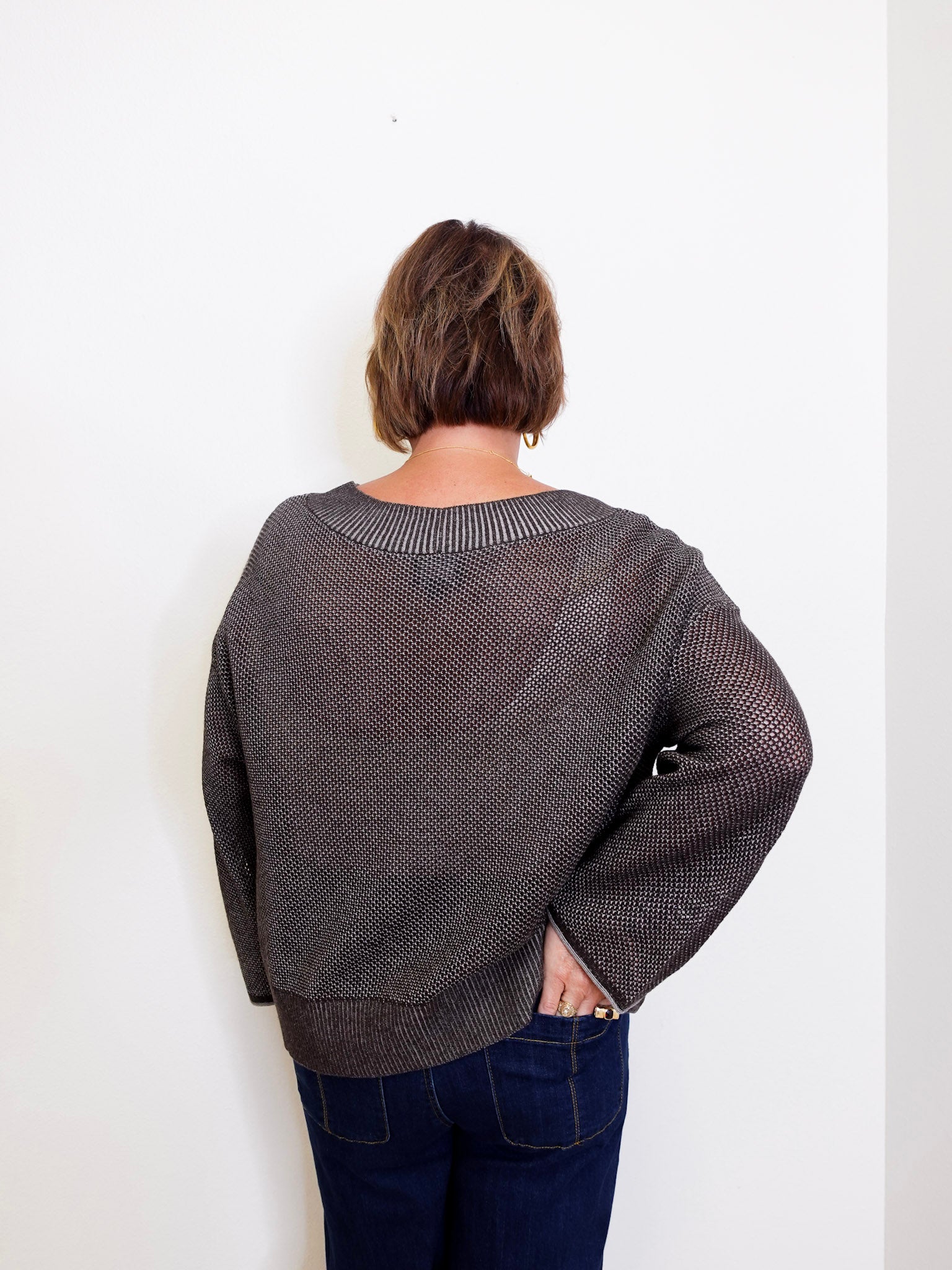 women wearing a brown sweater against a white wall. 