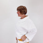 Woman wearing a white sweater with a yellow accent on a plain background