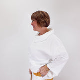 Woman wearing a white sweater with a yellow accent on a plain background