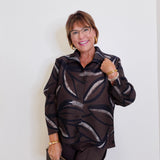 woman wearing a brown pleated top with brown pants in front of the background. 