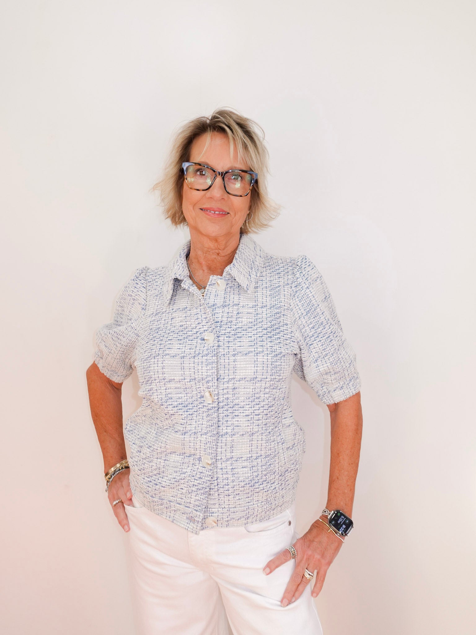 Person wearing a patterned shirt and white pants against a plain background