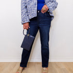 Person wearing a blue top, plaid jacket, and dark jeans against a white wall.