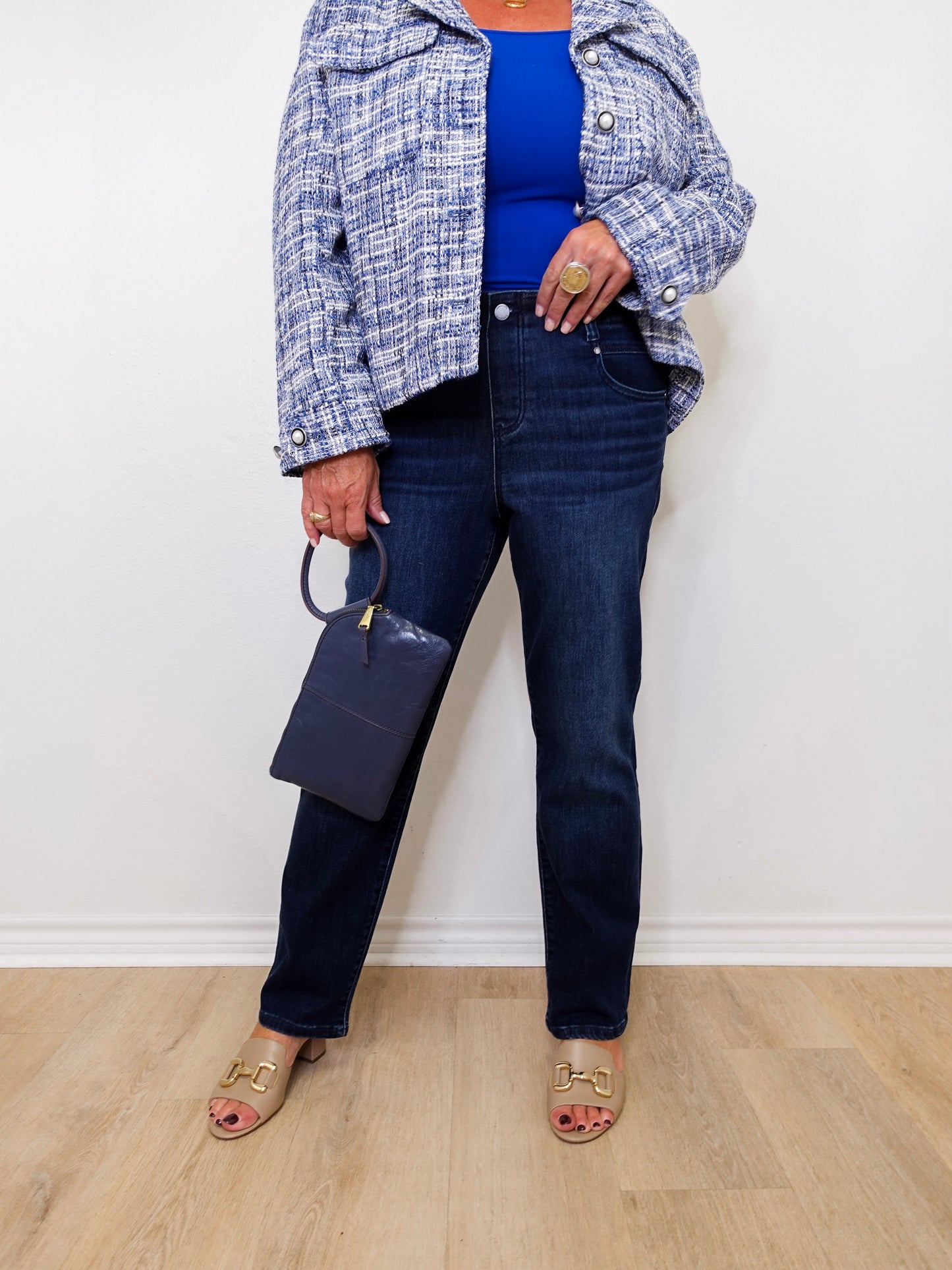 Person wearing a blue top, plaid jacket, and dark jeans against a white wall.