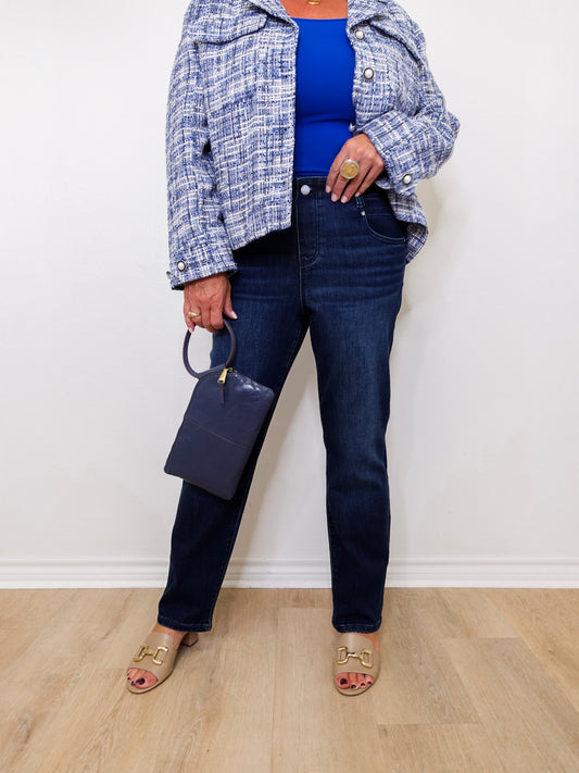 Person wearing a blue top, plaid jacket, and dark jeans against a white wall.