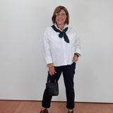 A woman modeling a white long-sleeve button-down shirt with a dark green patterned scarf, black pants, and dark gray peep-toe heels, standing against a plain white wall.