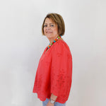 Woman wearing a red blouse with a colorful necklace against a white background