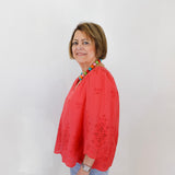 Woman wearing a red blouse with a colorful necklace against a white background