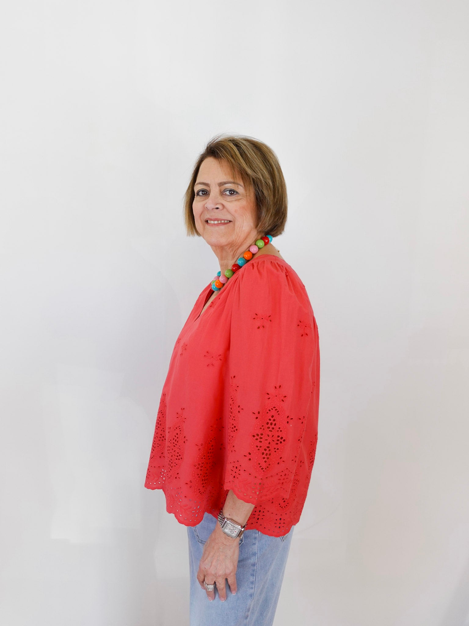 Woman wearing a red blouse with a colorful necklace against a white background