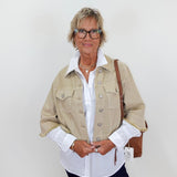 Woman wearing a beige jacket over a white shirt with a plain background