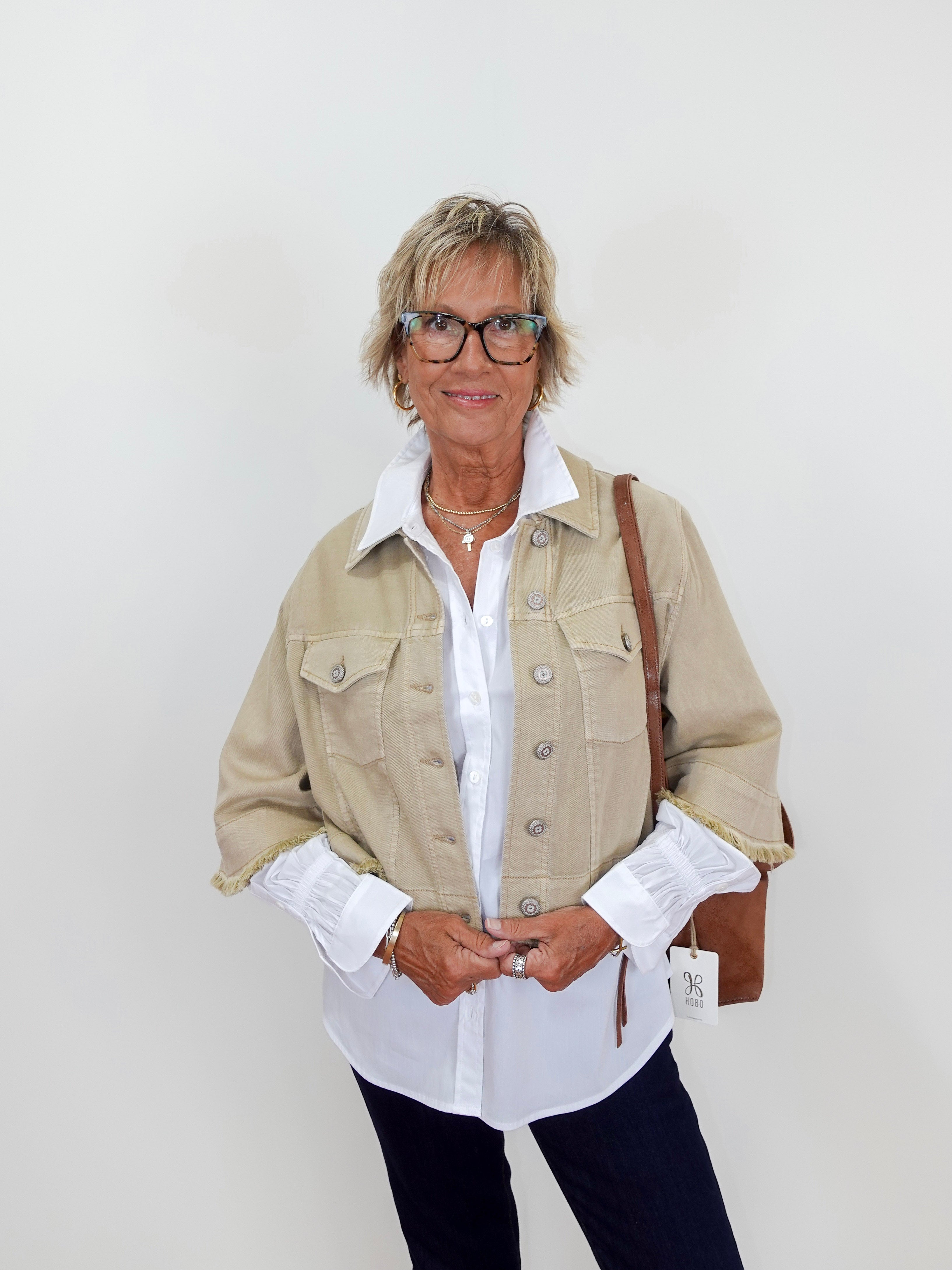 Woman wearing a beige jacket over a white shirt with a plain background