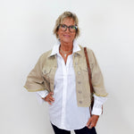 Woman wearing a beige jacket over a white shirt with a plain background