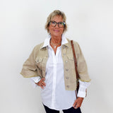 Woman wearing a beige jacket over a white shirt with a plain background