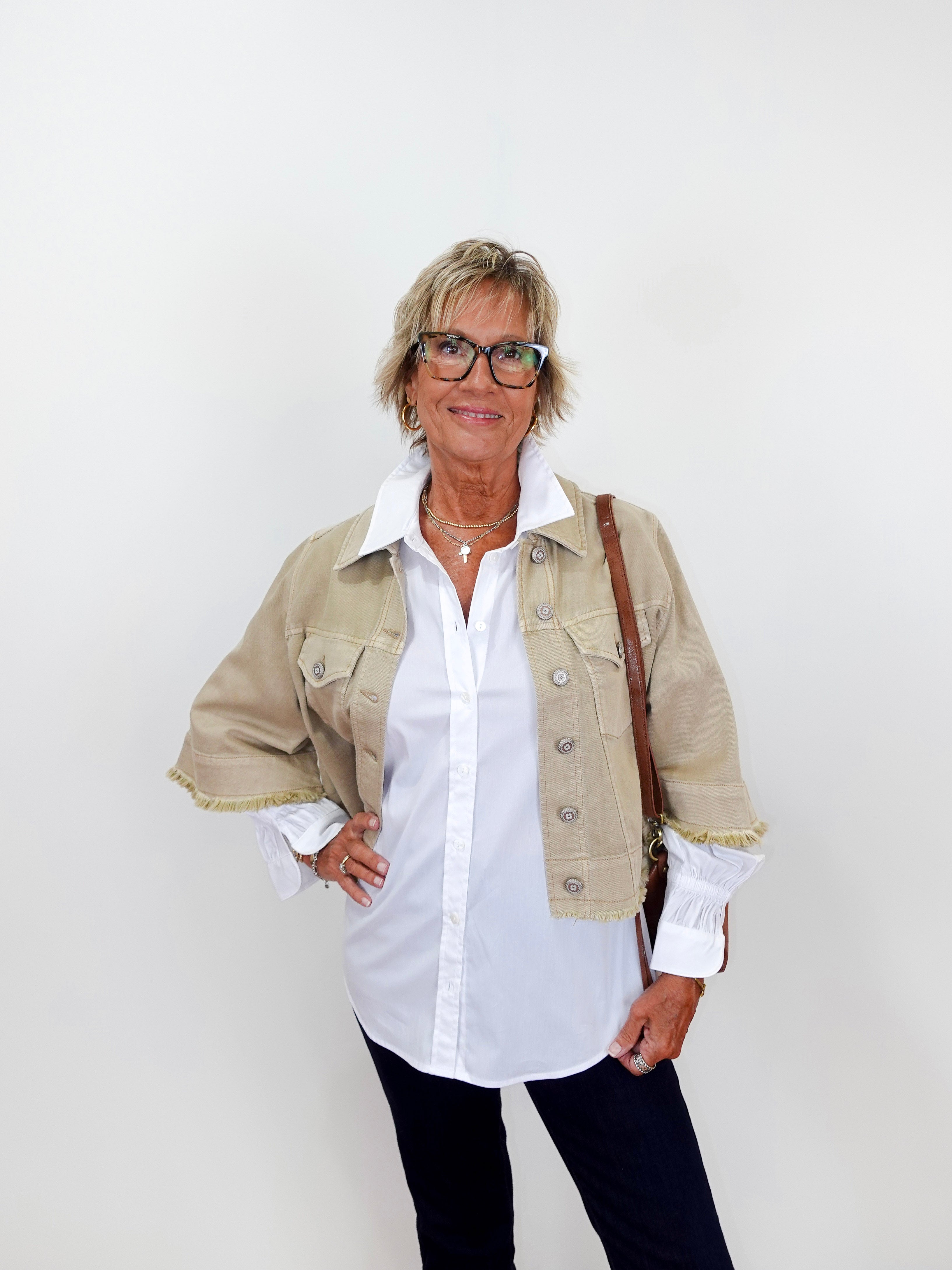 Woman wearing a beige jacket over a white shirt with a plain background
