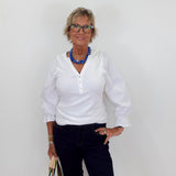Woman wearing a white blouse and dark pants against a plain background
