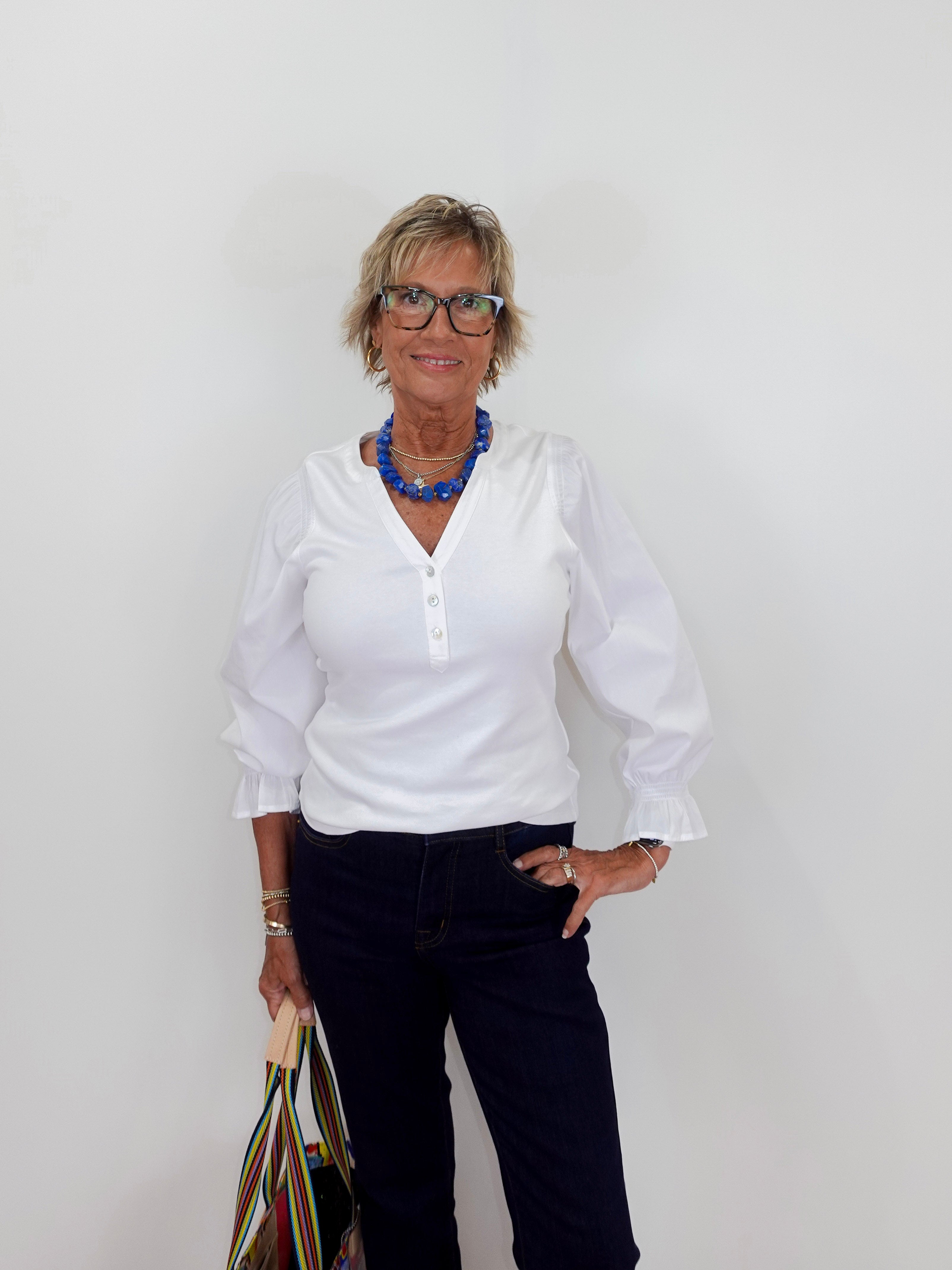 Woman wearing a white blouse and dark pants against a plain background