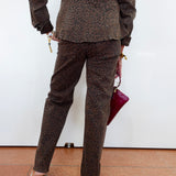 A person shown from the back wearing a matching brown leopard-print jacket and trousers, holding a magenta clutch against a plain white wall.