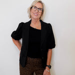 Woman wearing a black blazer, black top, and leopard print pants against a white background