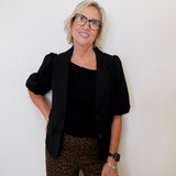 Woman wearing a black blazer, black top, and leopard print pants against a white background