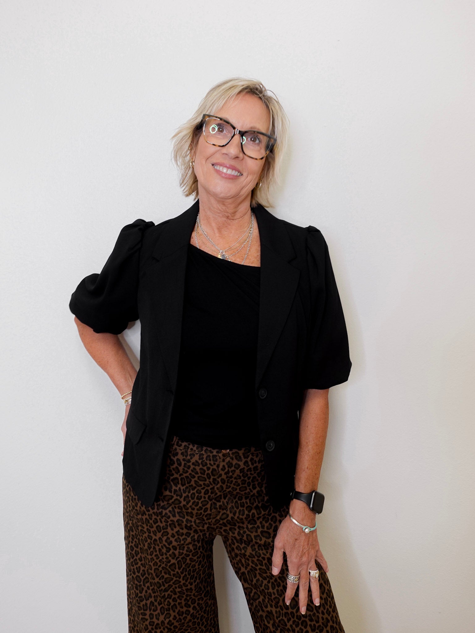 Woman wearing a black blazer, black top, and leopard print pants against a white background