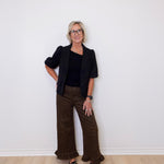 Woman wearing a black blazer and brown patterned pants against a white wall.