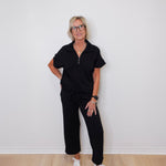 Person wearing a black outfit with white sneakers against a white wall