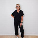 Person wearing a black outfit with white sneakers against a white wall