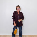 Woman wearing a dark blazer and jeans, holding a yellow handbag against a white wall.