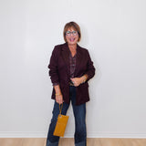 Woman wearing a dark blazer and jeans, holding a yellow handbag against a white wall.