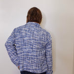 Person wearing a blue plaid shirt against a white wall