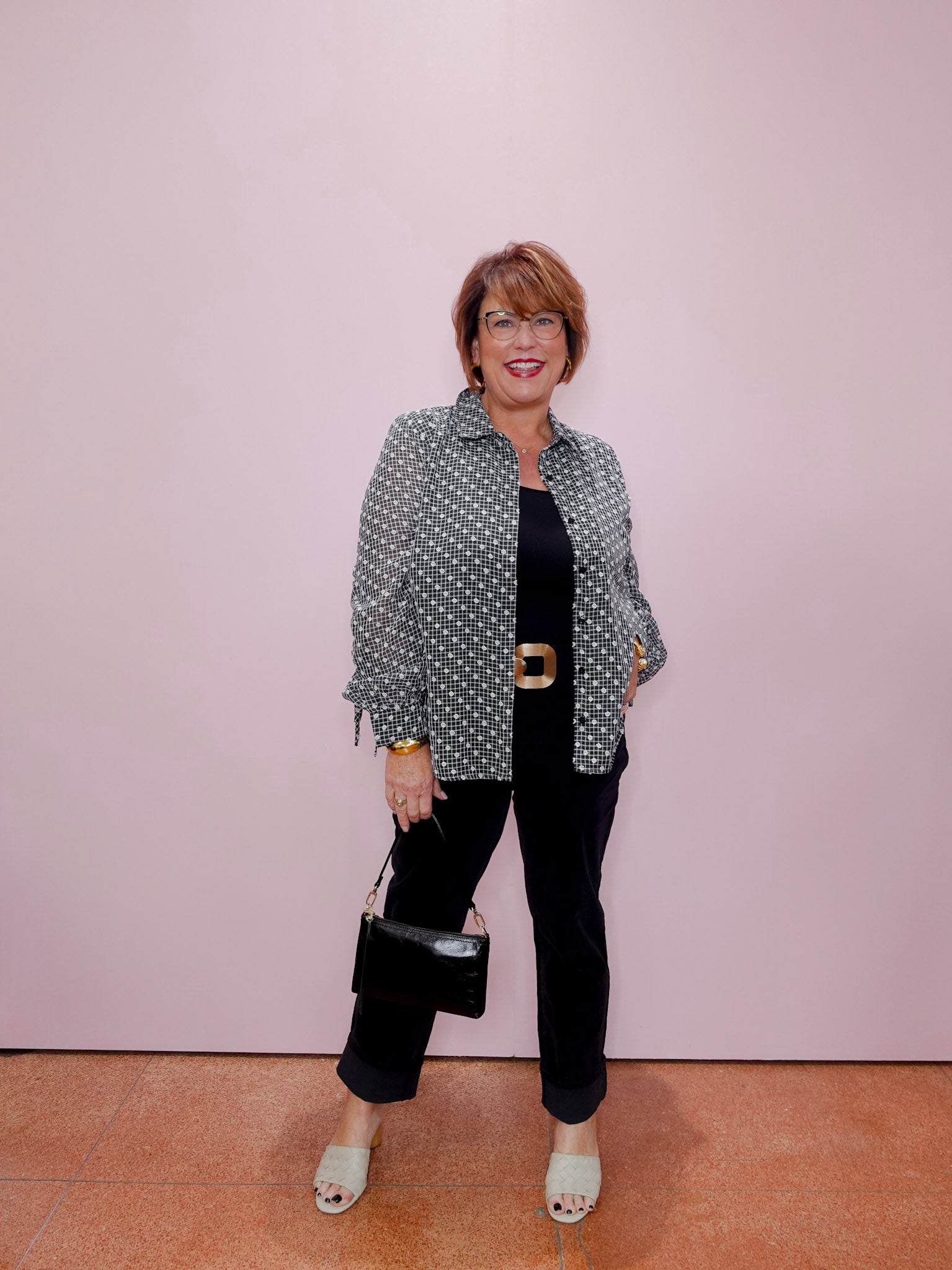 Woman wearing a polka dot shirt and black pants against a plain background
