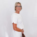 Woman in a white outfit holding a brown bag against a white background