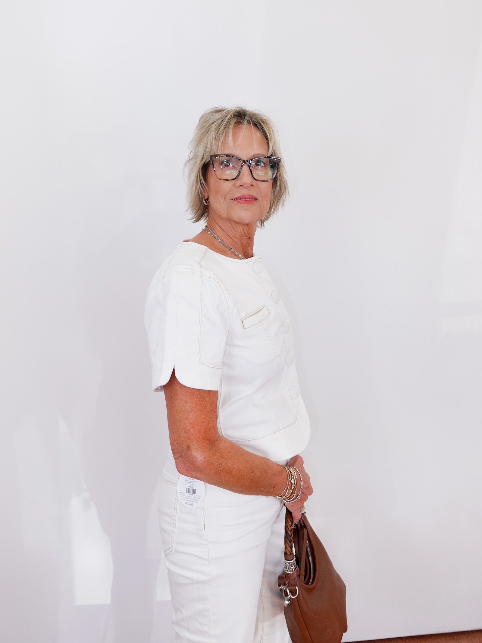 Woman in a white outfit holding a brown bag against a white background
