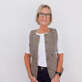 Woman wearing a patterned vest over a white shirt on a plain background