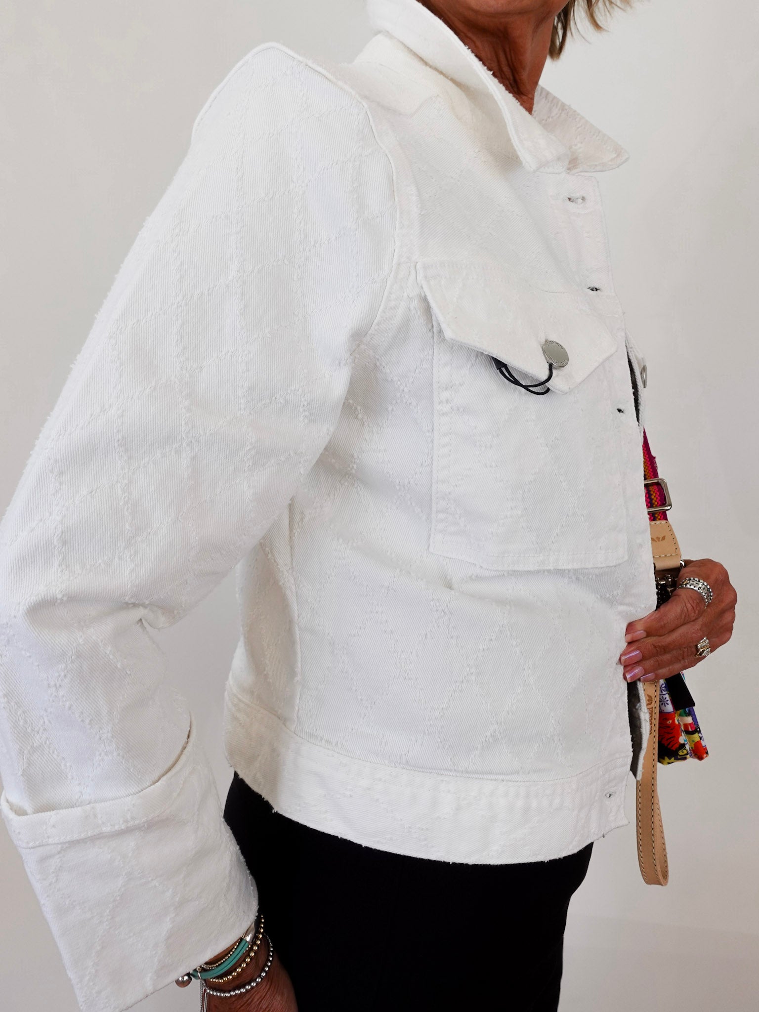Person wearing a white jacket holding a colorful bag against a plain background