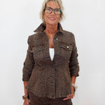 A woman with short blonde hair and glasses wearing a matching brown leopard-print jacket and trousers over a white top, standing against a plain white background.