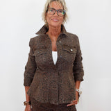 A woman with short blonde hair and glasses wearing a matching brown leopard-print jacket and trousers over a white top, standing against a plain white background.