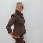 A woman with short gray hair and glasses wearing a brown leopard-print jacket and matching skirt, posing against a plain white wall.