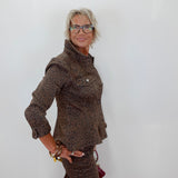 A woman with short gray hair and glasses wearing a brown leopard-print jacket and matching skirt, posing against a plain white wall.