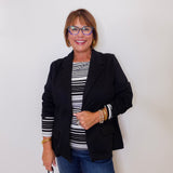Woman wearing a black blazer, striped shirt, and jeans against a white background