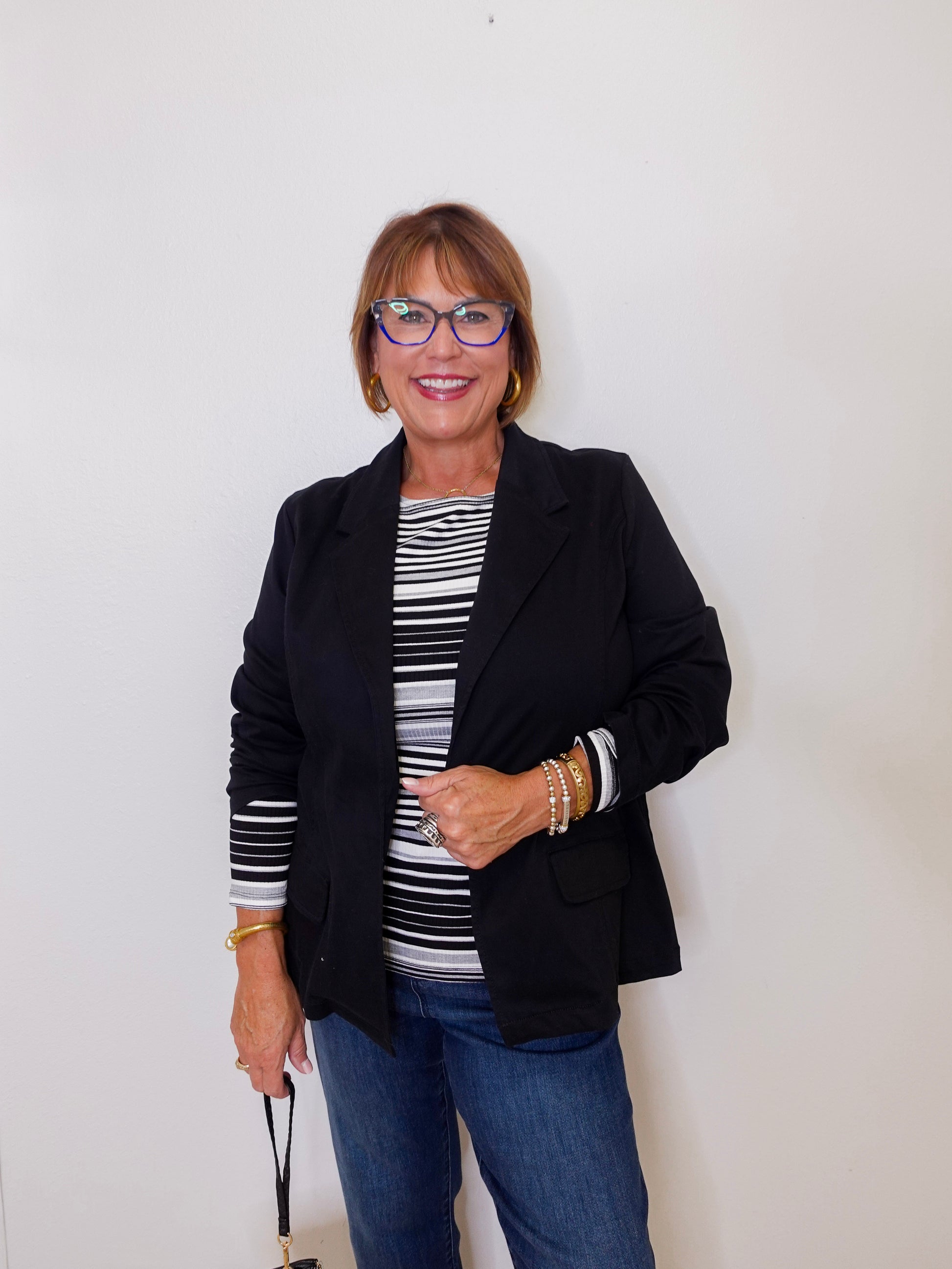 Woman wearing a black blazer, striped shirt, and jeans against a white background