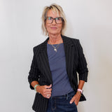 Woman wearing a black pinstripe blazer, blue shirt, and jeans against a white background