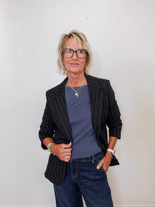 Woman wearing a black pinstripe blazer, blue shirt, and jeans against a white background