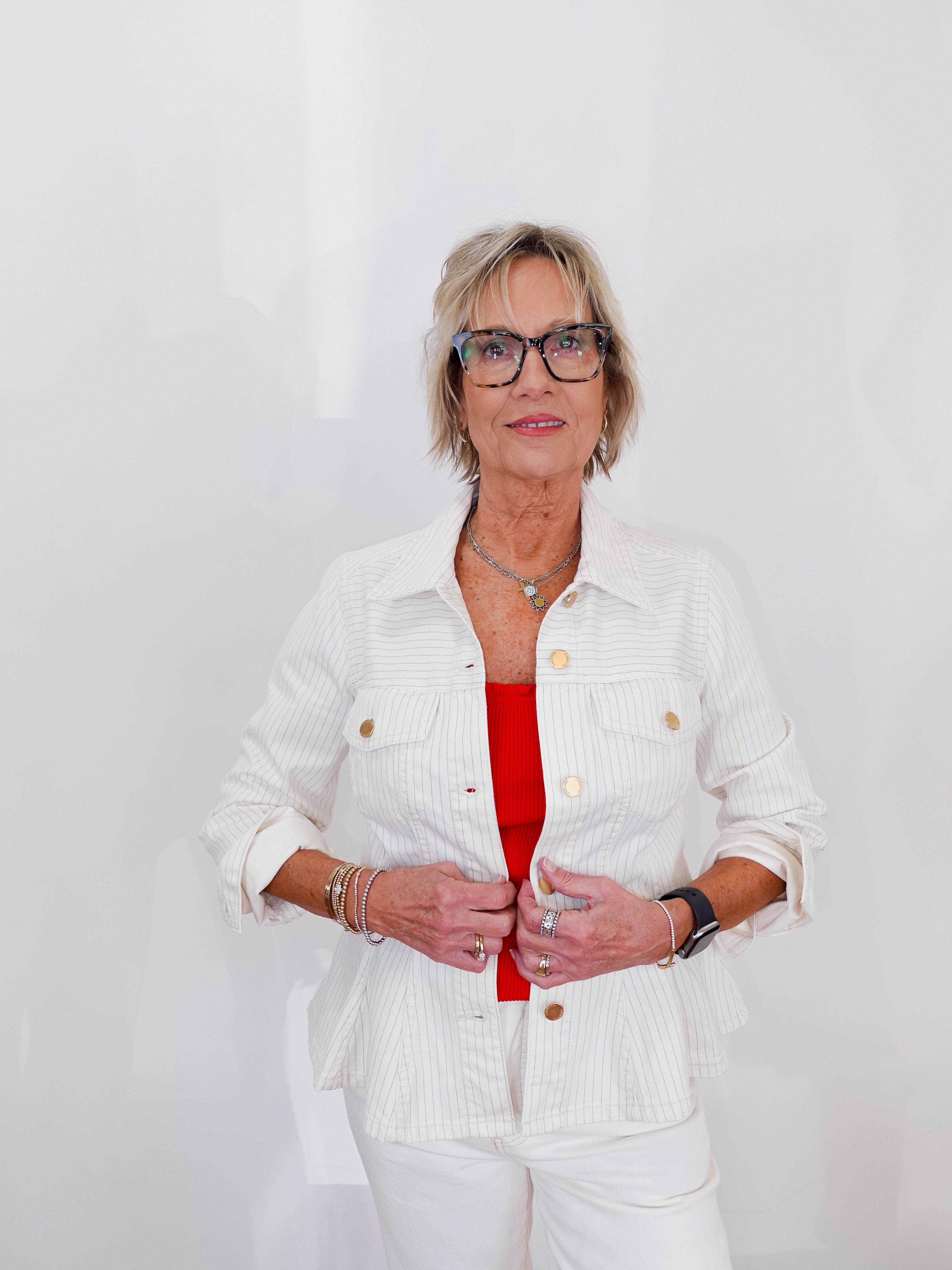 Woman wearing a white jacket over a red top on a plain background